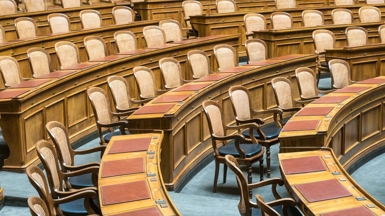 Empty legislative chamber with rows of wooden desks